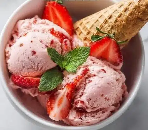 A bowl of homemade strawberry ice cream topped with fresh strawberries.